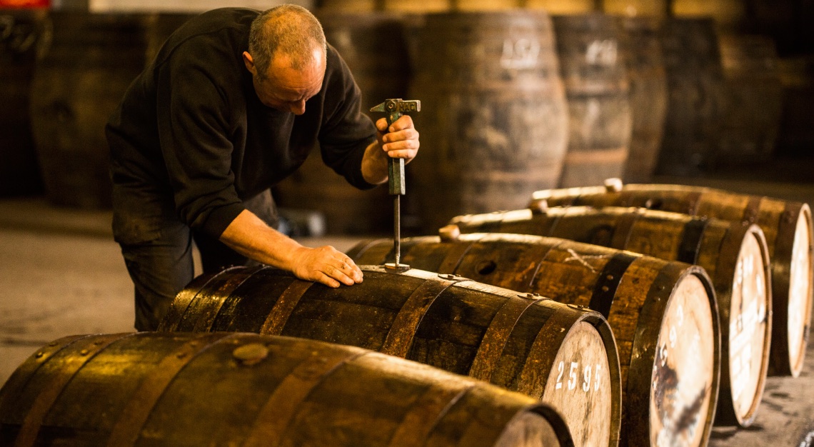 Male worker opening wooden whisky cask in whisky distillery in Scotland